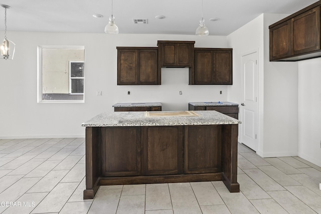 kitchen featuring pendant lighting, dark brown cabinetry, a center island, and light stone counters