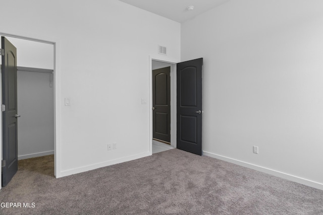 unfurnished bedroom with a walk in closet, light colored carpet, and a closet