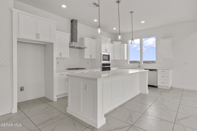 kitchen with appliances with stainless steel finishes, decorative light fixtures, white cabinets, a center island, and wall chimney range hood