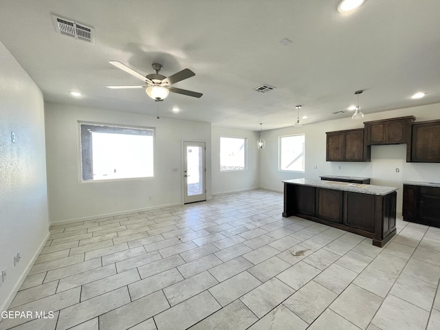 kitchen featuring ceiling fan with notable chandelier, light stone countertops, dark brown cabinetry, a center island, and light tile patterned flooring