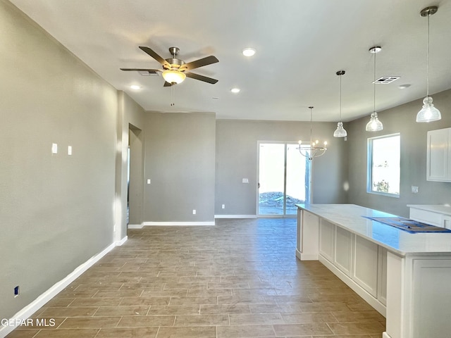 kitchen featuring ceiling fan with notable chandelier, light stone counters, pendant lighting, and white cabinets