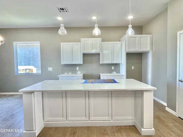 kitchen featuring white cabinetry, pendant lighting, a center island, and light stone countertops