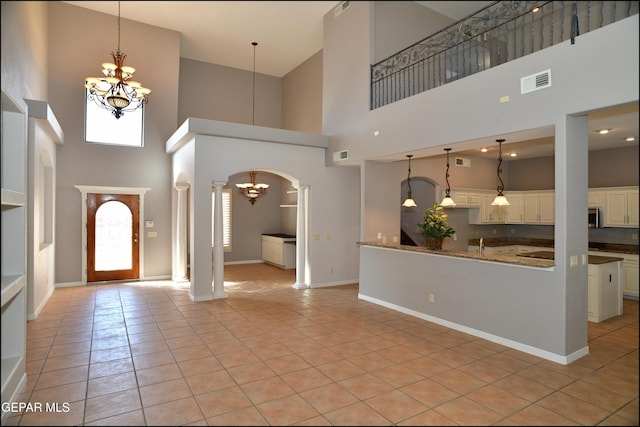 tiled foyer entrance featuring ornate columns, a towering ceiling, and a chandelier