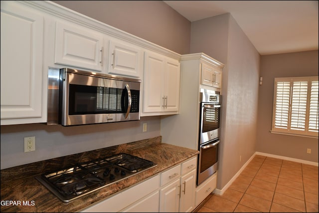 kitchen with white cabinets, light tile patterned floors, appliances with stainless steel finishes, and dark stone counters