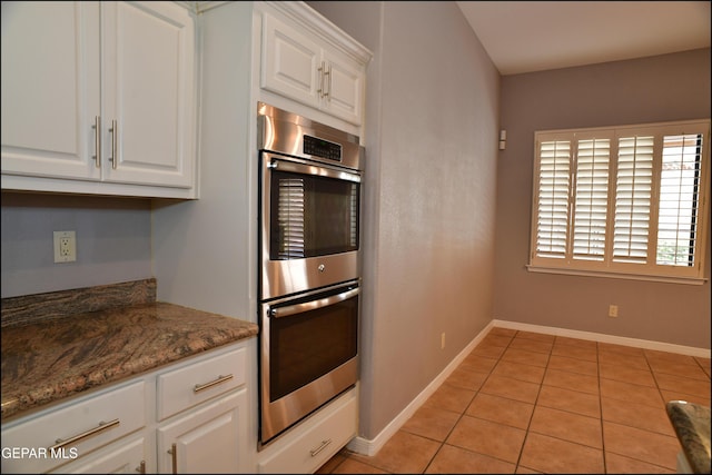 kitchen featuring white cabinets, dark stone countertops, stainless steel double oven, and light tile patterned floors