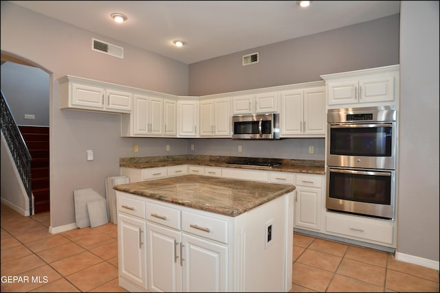 kitchen featuring white cabinetry, stainless steel appliances, a kitchen island, dark stone countertops, and light tile patterned flooring