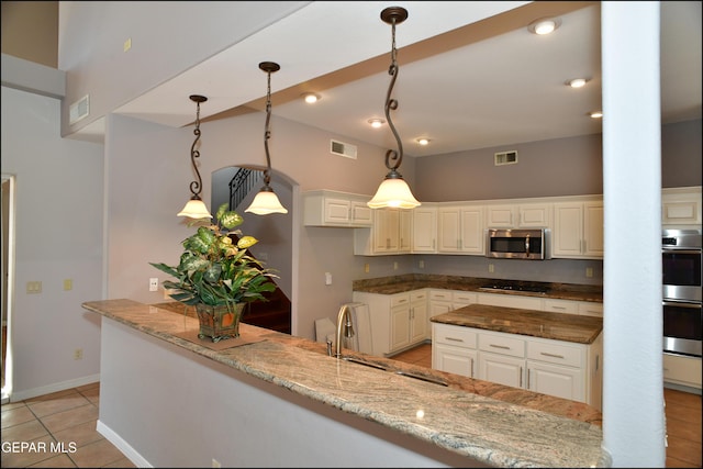 kitchen featuring appliances with stainless steel finishes, dark stone counters, pendant lighting, light tile patterned floors, and white cabinets