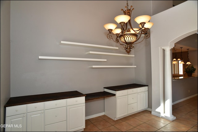 unfurnished dining area featuring a chandelier, light tile patterned floors, and ornate columns