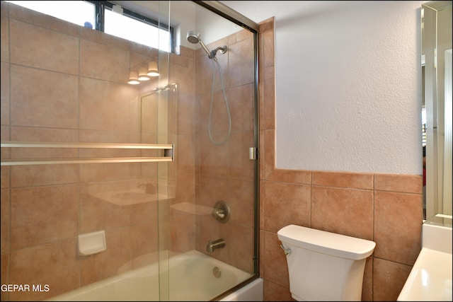 full bathroom with shower / bath combination with glass door, vanity, tile walls, and toilet