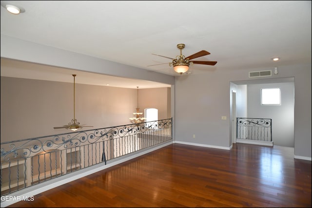 unfurnished room with ceiling fan with notable chandelier and dark hardwood / wood-style flooring