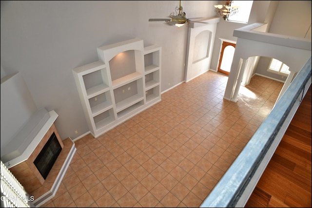 tiled entryway featuring ceiling fan with notable chandelier, a towering ceiling, and a tiled fireplace