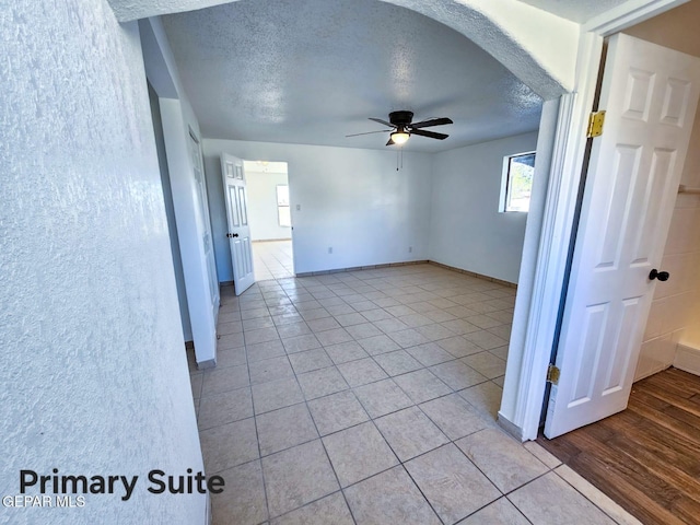 empty room featuring ceiling fan, light tile patterned floors, and a textured ceiling