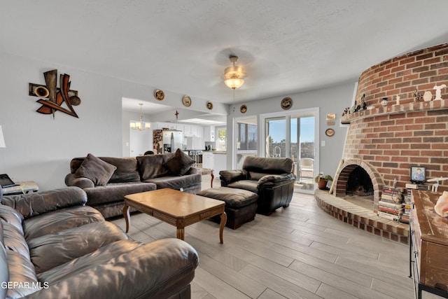 living room featuring a fireplace, light hardwood / wood-style floors, and ceiling fan with notable chandelier