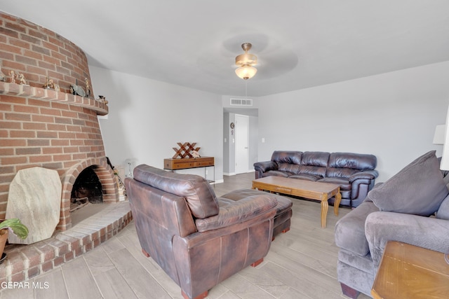 living room with a brick fireplace, ceiling fan, and light hardwood / wood-style flooring