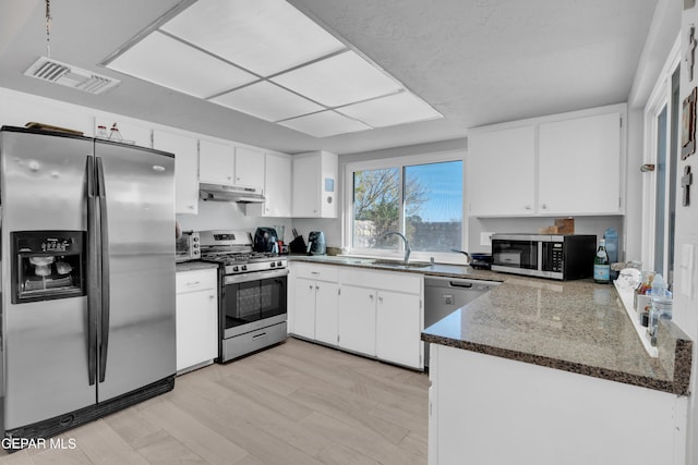 kitchen with dark stone counters, sink, light wood-type flooring, appliances with stainless steel finishes, and white cabinetry