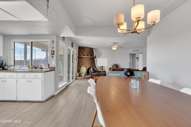 dining space featuring a fireplace, light hardwood / wood-style floors, and ceiling fan with notable chandelier