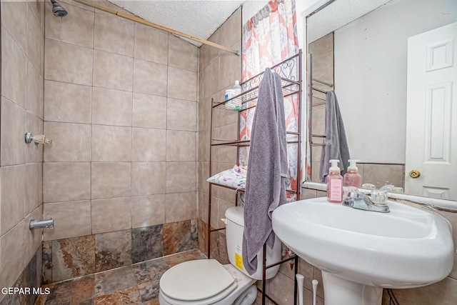 bathroom featuring a textured ceiling, sink, toilet, and tiled shower