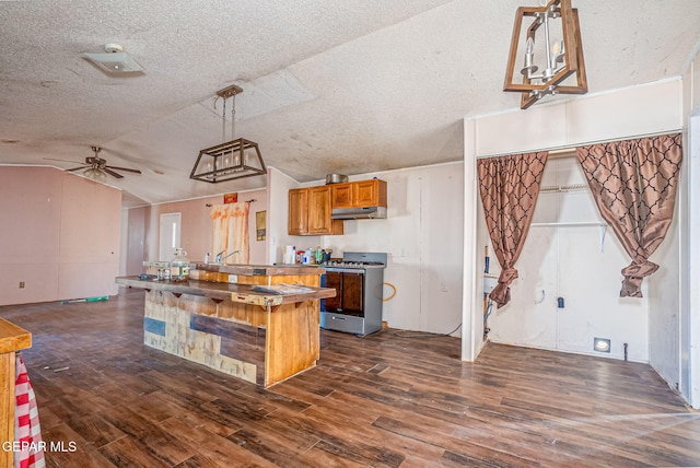 kitchen with ceiling fan, stainless steel gas stove, dark hardwood / wood-style flooring, pendant lighting, and lofted ceiling