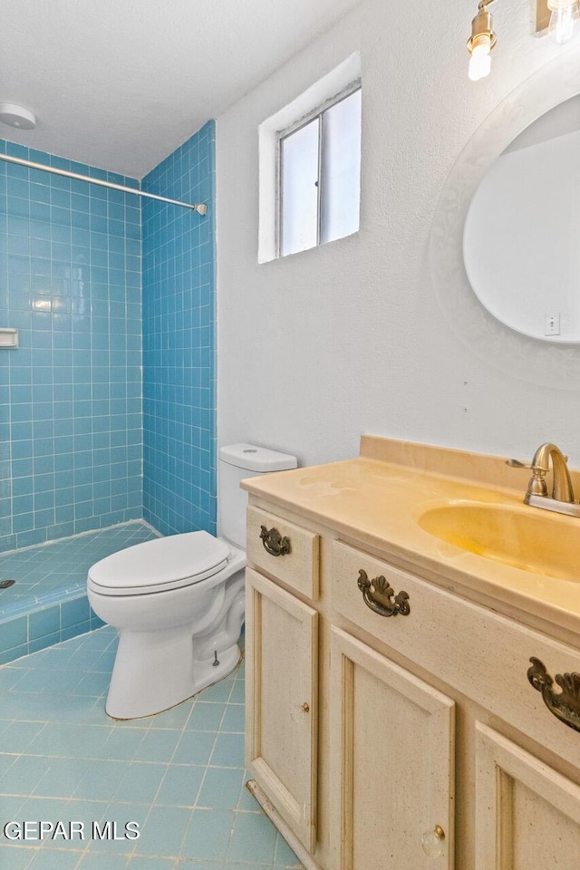 bathroom with tile patterned flooring, vanity, toilet, and tiled shower