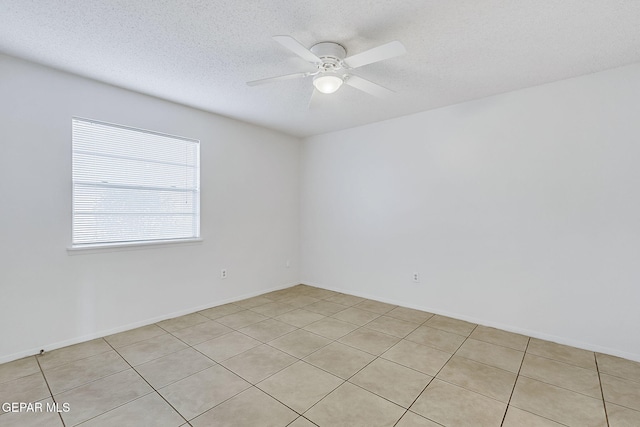 spare room featuring ceiling fan, light tile patterned floors, and a textured ceiling