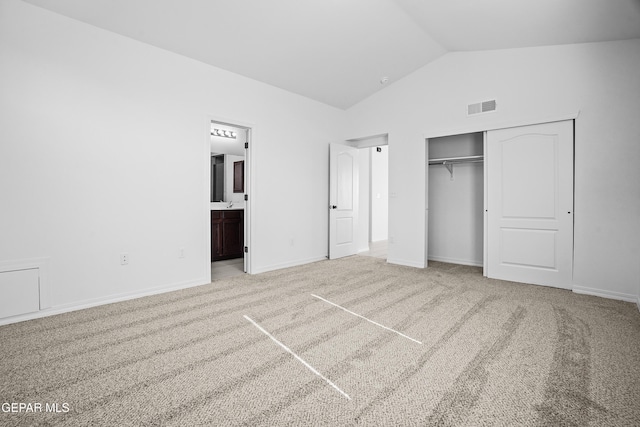 unfurnished bedroom with connected bathroom, a closet, light colored carpet, and vaulted ceiling