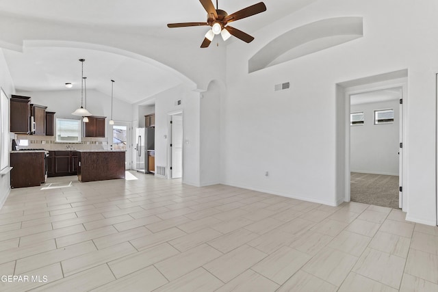 unfurnished living room with ceiling fan, light tile patterned floors, and vaulted ceiling