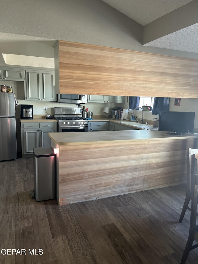 kitchen with sink, dark wood-type flooring, kitchen peninsula, a textured ceiling, and appliances with stainless steel finishes