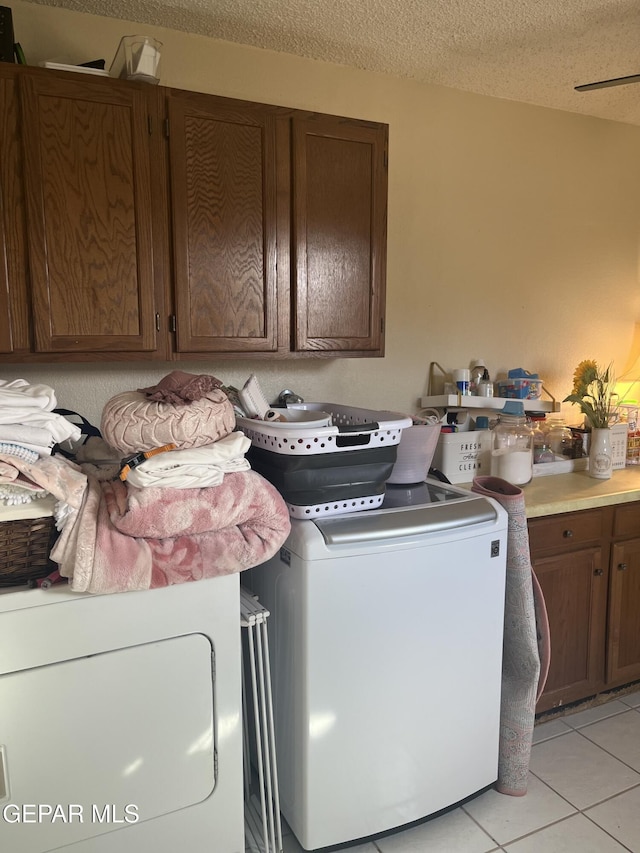 clothes washing area with light tile patterned flooring, cabinets, a textured ceiling, and washing machine and dryer