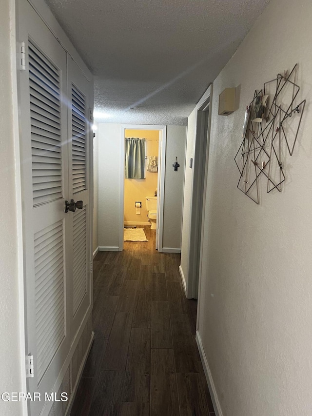 corridor with a textured ceiling and dark wood-type flooring