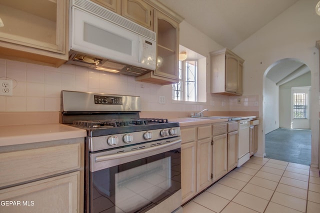 kitchen featuring sink, cream cabinetry, vaulted ceiling, white appliances, and light tile patterned floors