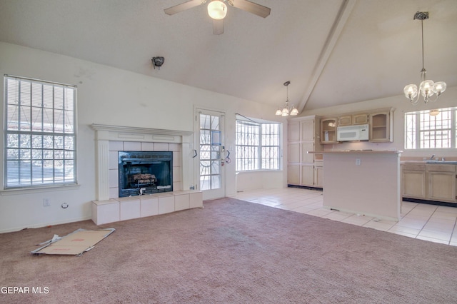 unfurnished living room with ceiling fan with notable chandelier, light tile patterned floors, high vaulted ceiling, beamed ceiling, and a tiled fireplace