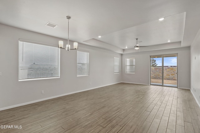 unfurnished room with ceiling fan with notable chandelier and a raised ceiling