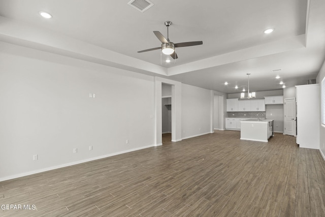 unfurnished living room with ceiling fan, wood-type flooring, sink, and a tray ceiling