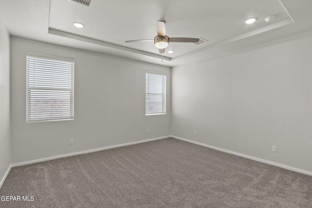 carpeted spare room with a raised ceiling and ceiling fan