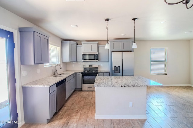 kitchen with sink, a center island, light hardwood / wood-style floors, pendant lighting, and appliances with stainless steel finishes