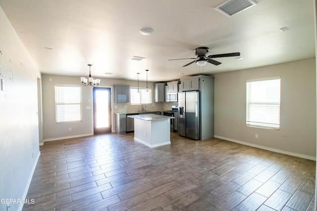 kitchen featuring gray cabinetry, a center island, ceiling fan with notable chandelier, hanging light fixtures, and appliances with stainless steel finishes