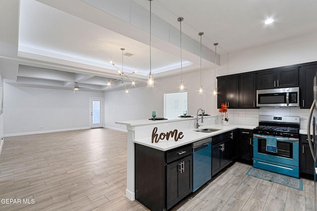 kitchen featuring sink, ceiling fan, appliances with stainless steel finishes, a tray ceiling, and kitchen peninsula