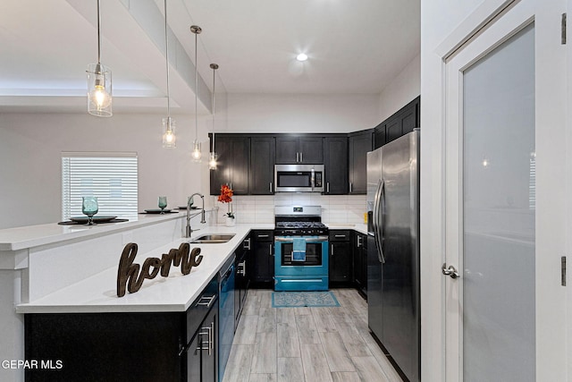 kitchen featuring kitchen peninsula, appliances with stainless steel finishes, light wood-type flooring, sink, and decorative light fixtures