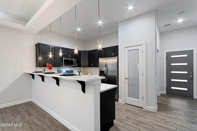 kitchen featuring a kitchen breakfast bar, backsplash, kitchen peninsula, decorative light fixtures, and appliances with stainless steel finishes