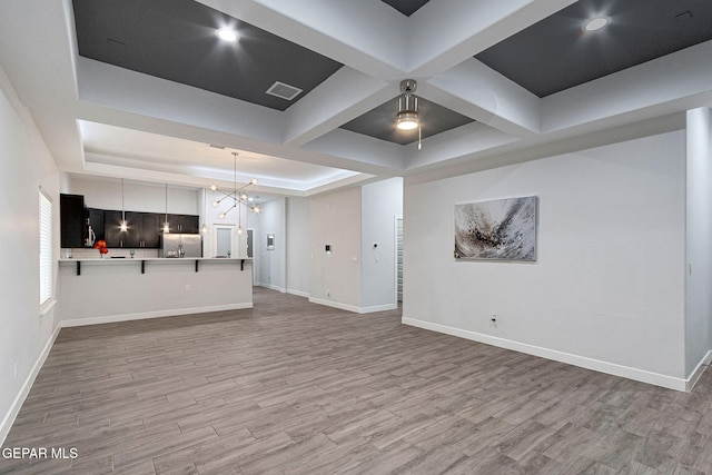 unfurnished living room featuring a tray ceiling, an inviting chandelier, and light hardwood / wood-style floors