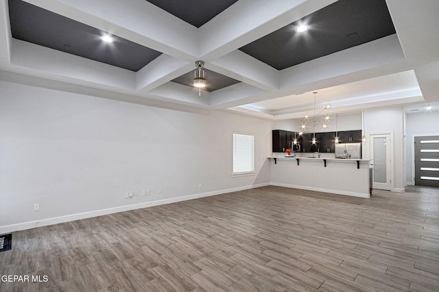 unfurnished living room featuring an inviting chandelier, light hardwood / wood-style floors, and a raised ceiling