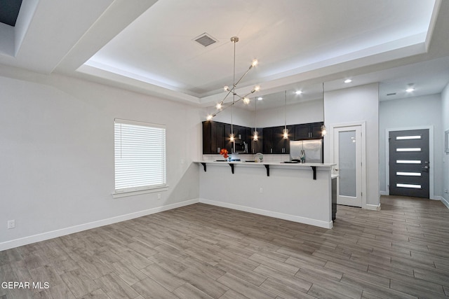 kitchen featuring kitchen peninsula, appliances with stainless steel finishes, a breakfast bar, a raised ceiling, and decorative light fixtures