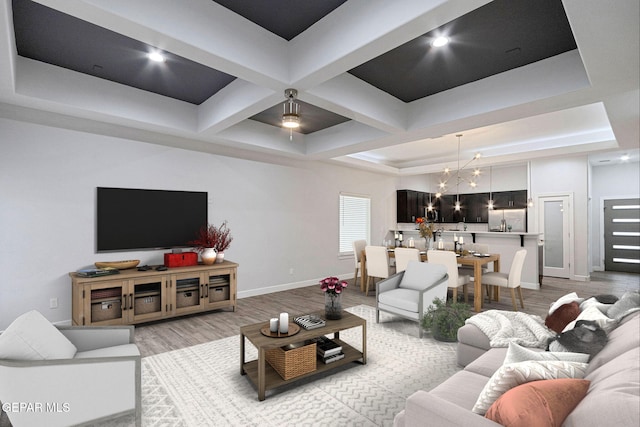 living room with a notable chandelier, a raised ceiling, and light hardwood / wood-style flooring