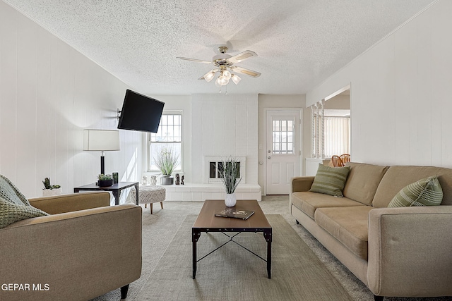 carpeted living room featuring a large fireplace, a textured ceiling, and ceiling fan