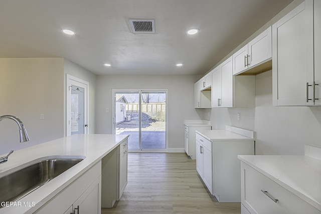 kitchen featuring white cabinetry, sink, light stone counters, and light wood-type flooring