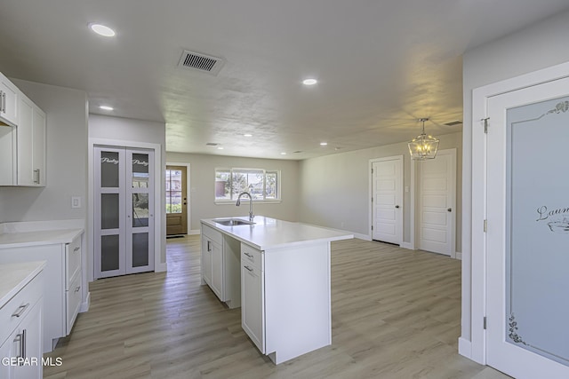 kitchen with light wood-type flooring, a center island with sink, white cabinetry, and sink