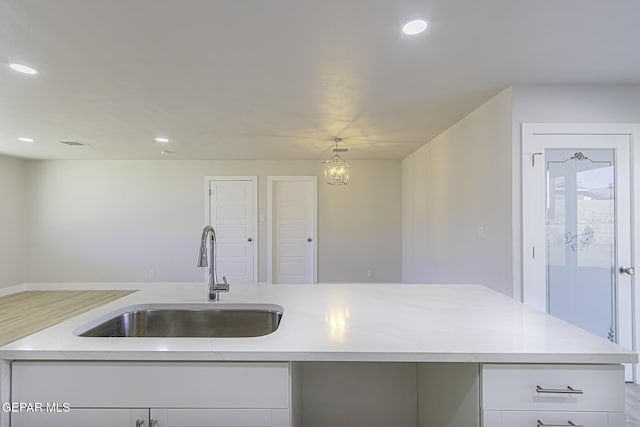 kitchen with sink, decorative light fixtures, a notable chandelier, white cabinetry, and an island with sink