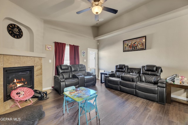 living room with ceiling fan, a tiled fireplace, and dark hardwood / wood-style flooring