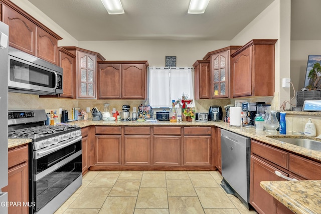 kitchen with tasteful backsplash, sink, light stone countertops, appliances with stainless steel finishes, and light tile patterned floors