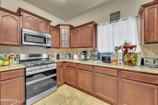 kitchen with light stone counters, light tile patterned floors, stainless steel appliances, and tasteful backsplash